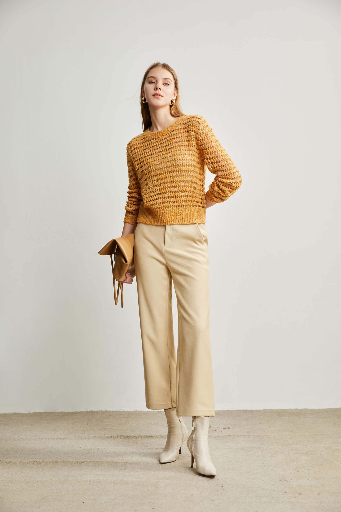 A woman wearing a yellow eyelet stitch sweater and holding a delicate bag