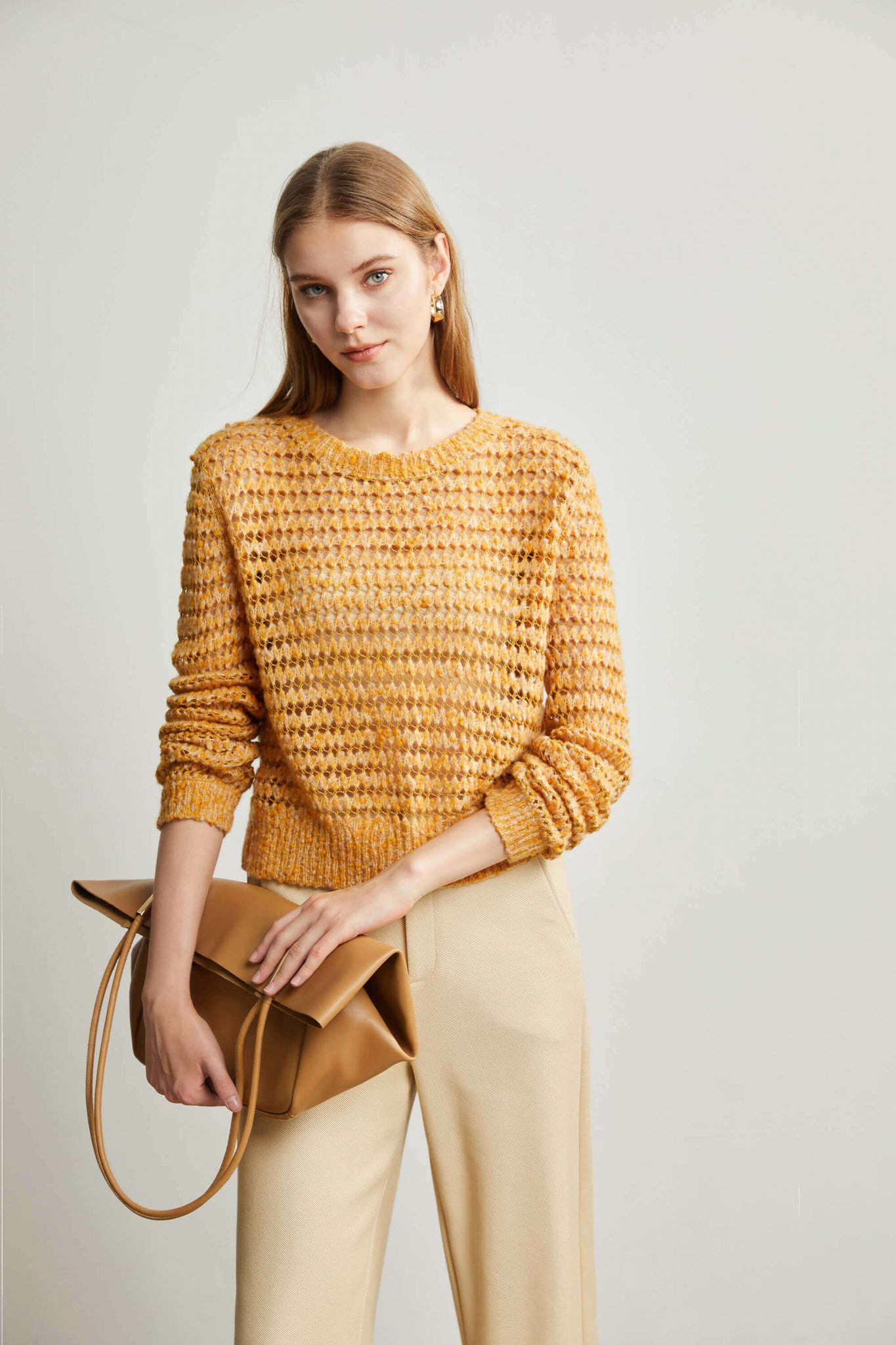 A woman wearing a yellow eyelet stitch sweater and holding a delicate bag