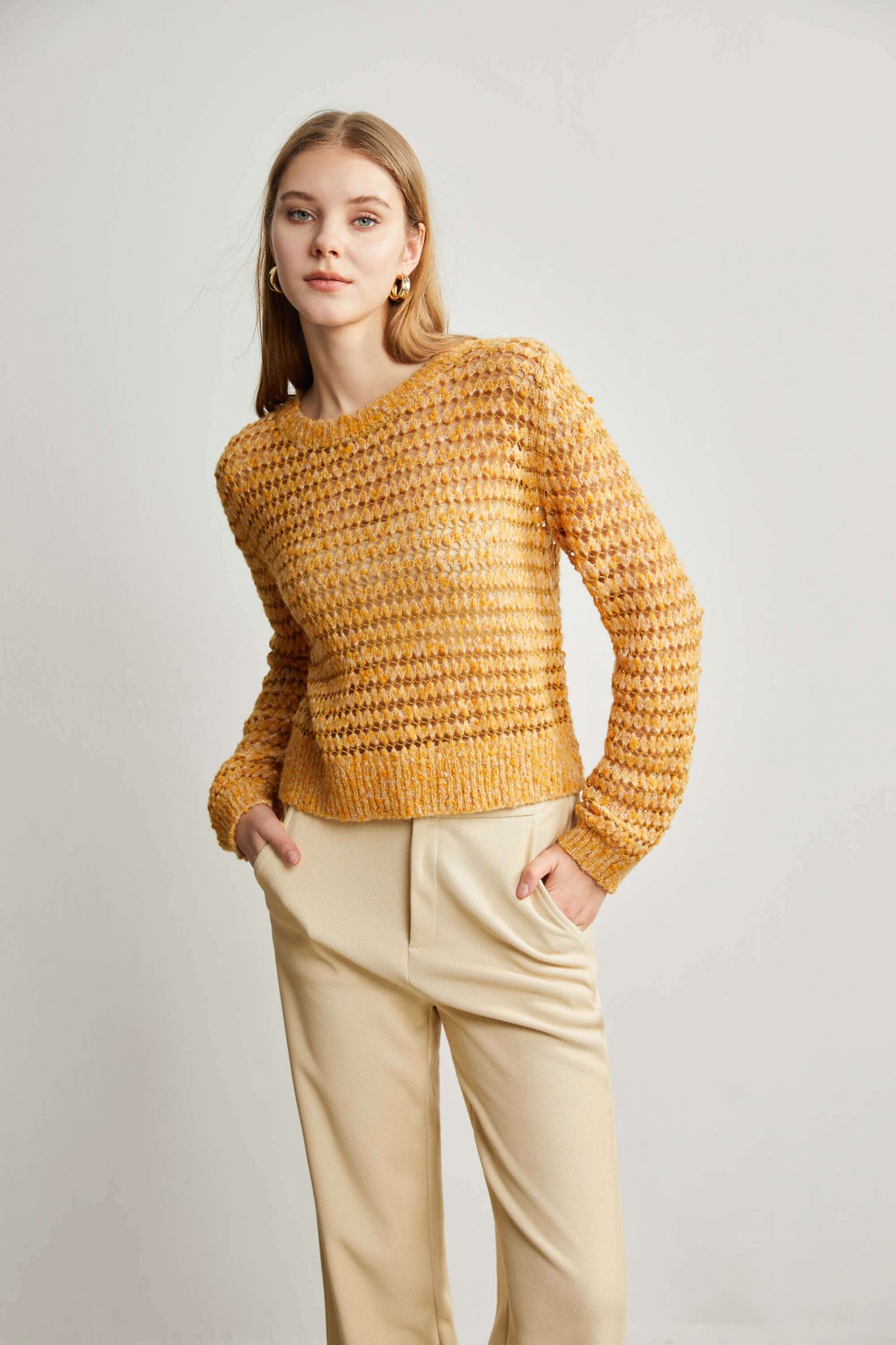 A woman wearing a yellow sweater with eyelet stitch, with her hands in her pockets