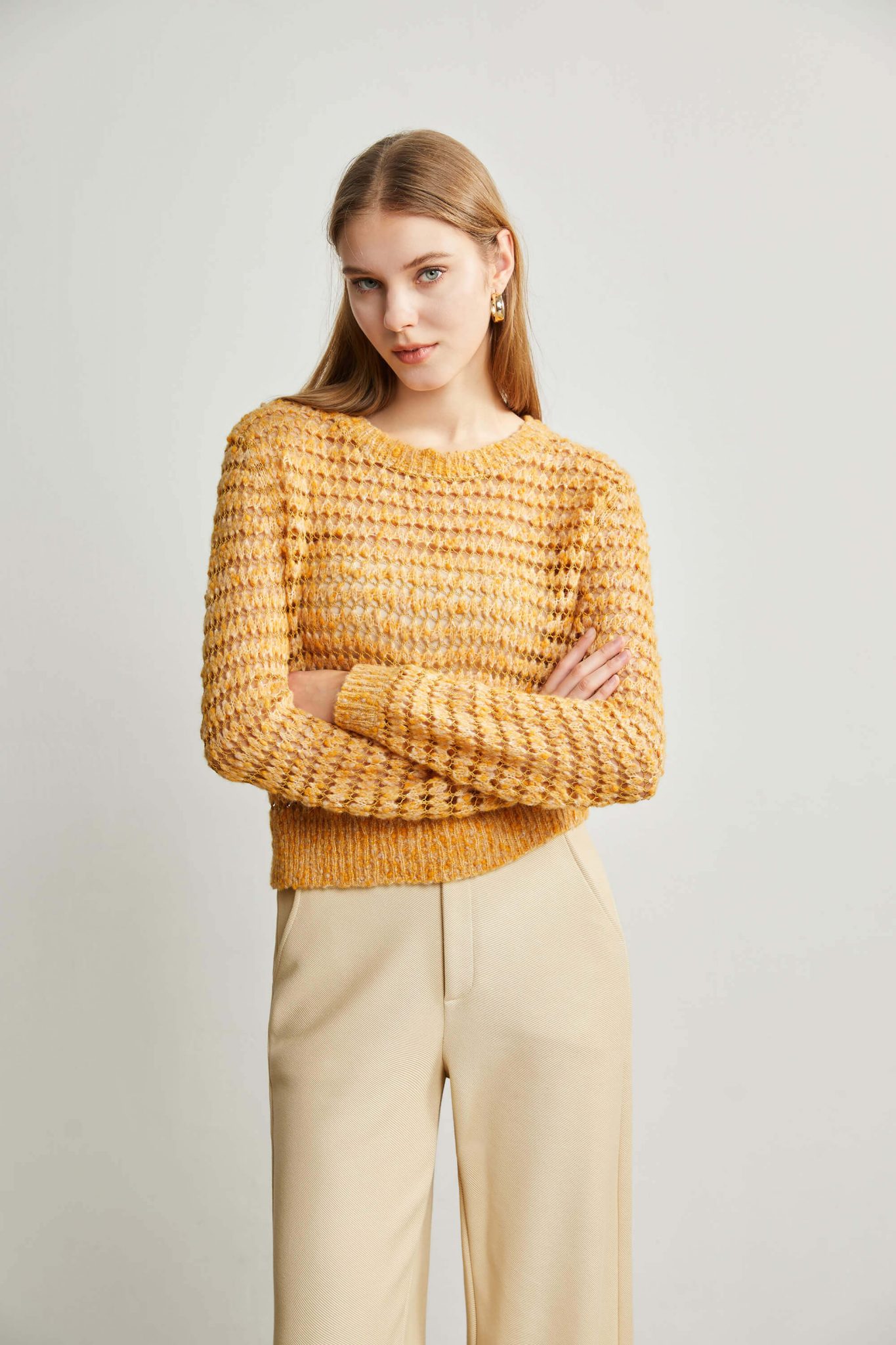 A woman wearing a yellow eyelet stitch sweater with her hands folded across her chest