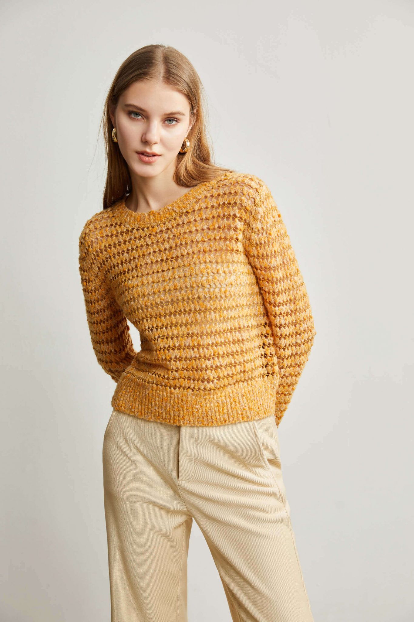 A woman wearing a yellow sweater with a pointelle stitch pattern with her hands behind her back