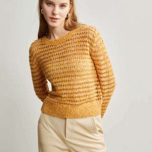 A woman wearing a yellow sweater with a pointelle stitch pattern with her hands behind her back