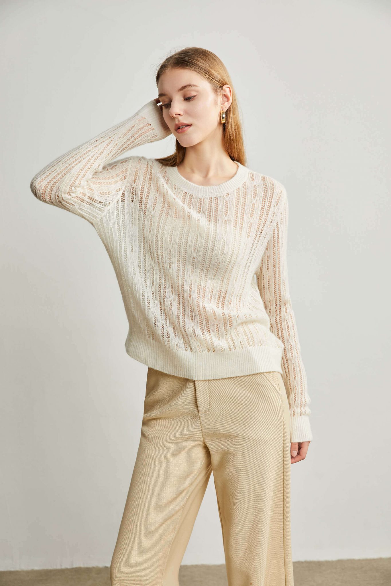 A woman wearing a white pointelle-stitch knitted top, touching her face with her right hand