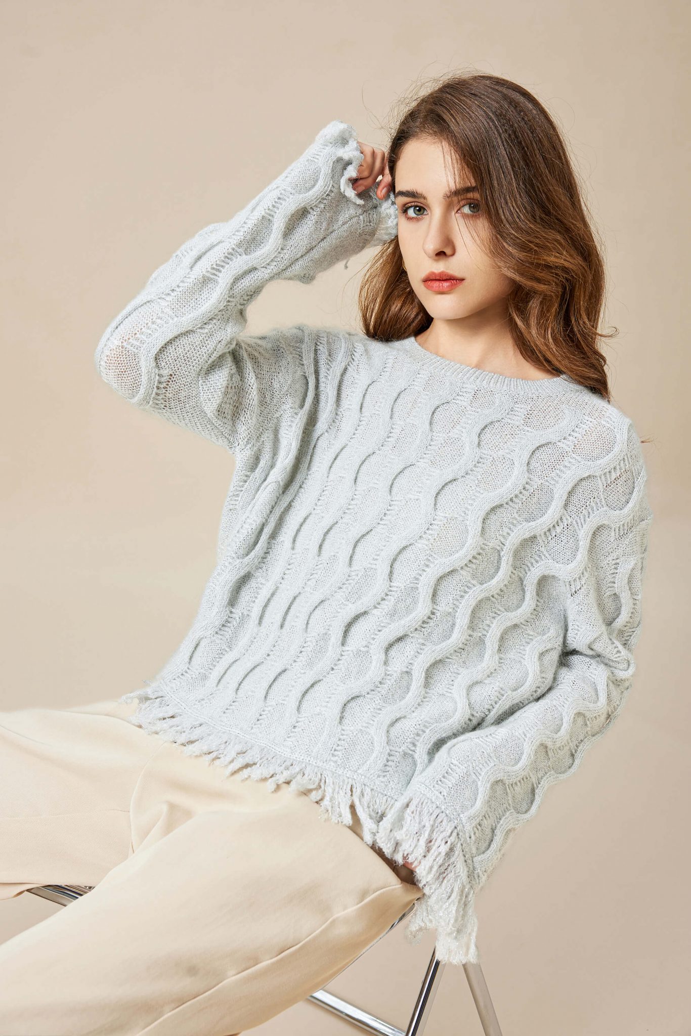 A girl wearing a mohair wool blend Lurex knitted pullover with tassels, sitting lazily in a chair