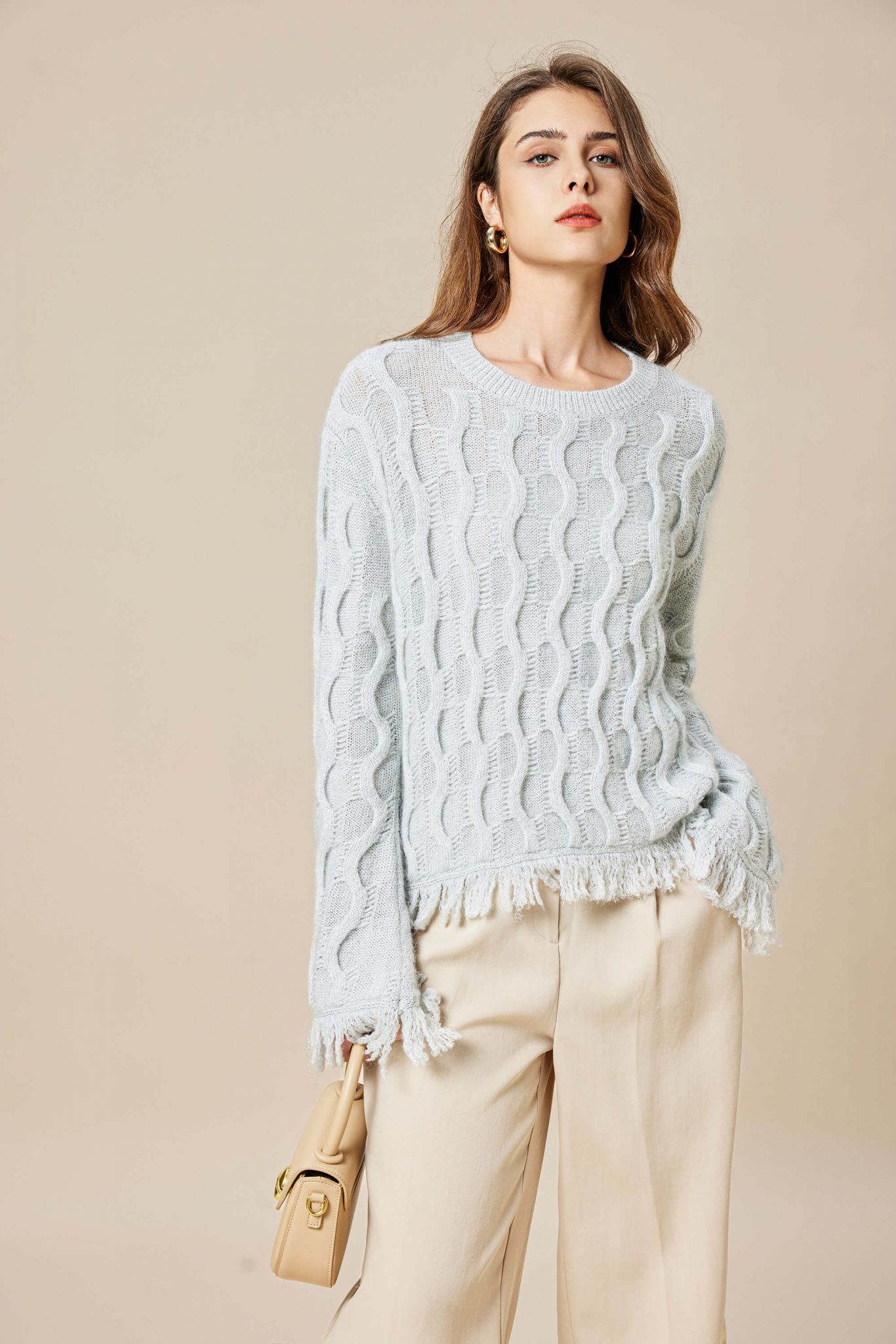 A girl wearing a mohair wool blend Lurex knitted pullover with tassels, holding a bag in her right hand and her left hand in her pocket