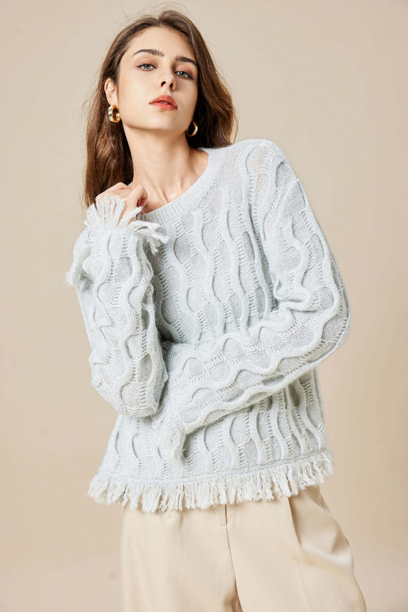 A girl wearing a mohair wool blend Lurex knitted pullover with tassels, touching her round collar with her right hand coolly