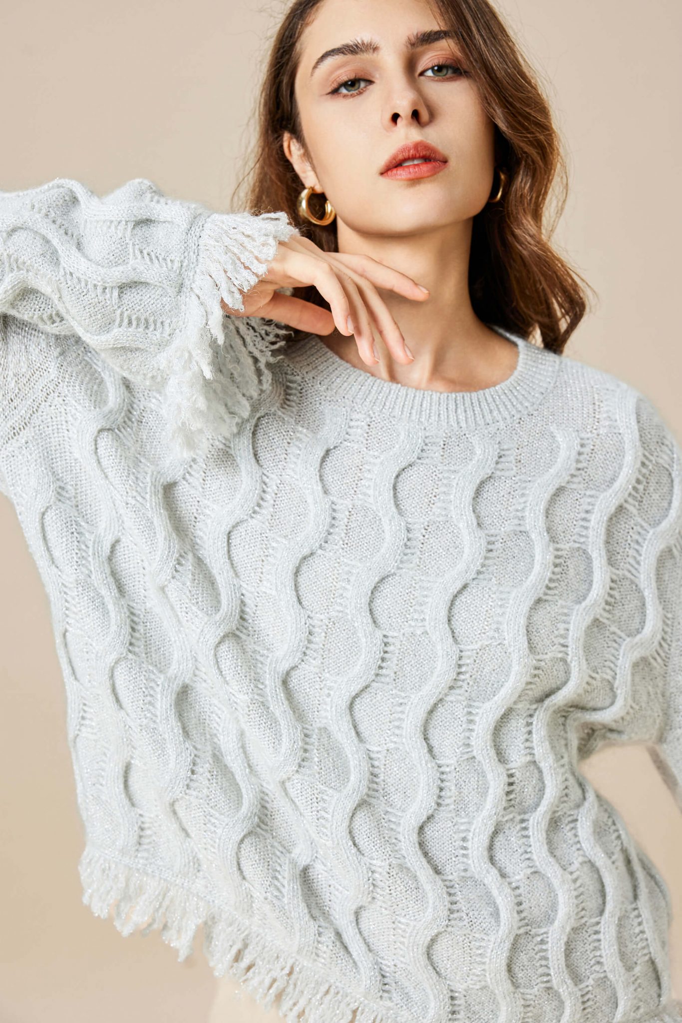 A girl wearing a mohair wool blend Lurex knitted pullover with tassels, showing her round collar with her right hand coolly